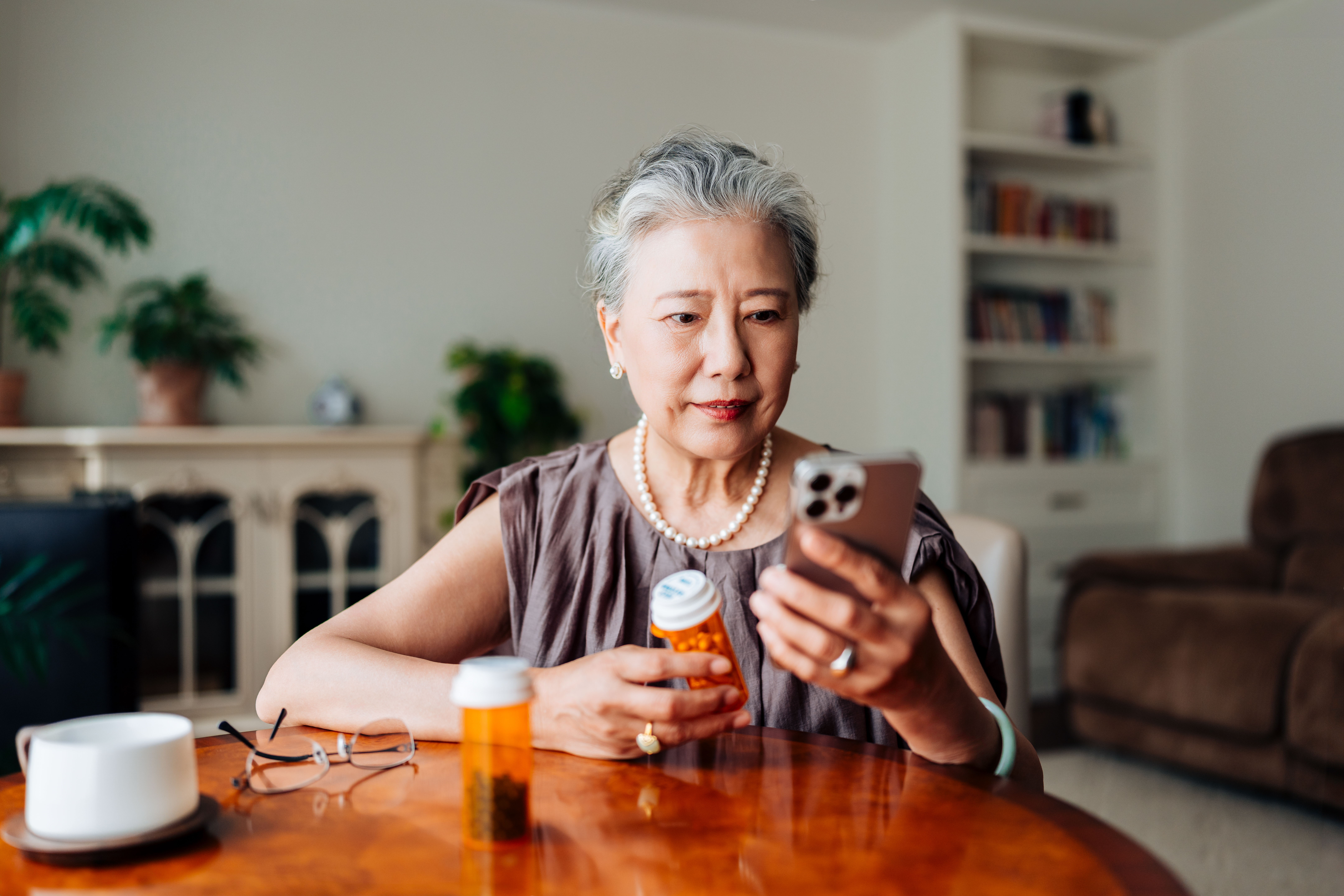 Asian senior woman having a virtual appointment with doctor online, consulting her prescription and choice of medication on smartphone at home. Telemedicine, elderly and healthcare concept.