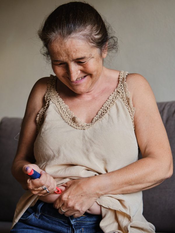 front view portrait of a white European generation X woman pricking her belly with an insulin pen to take care of her sugar levels indoors